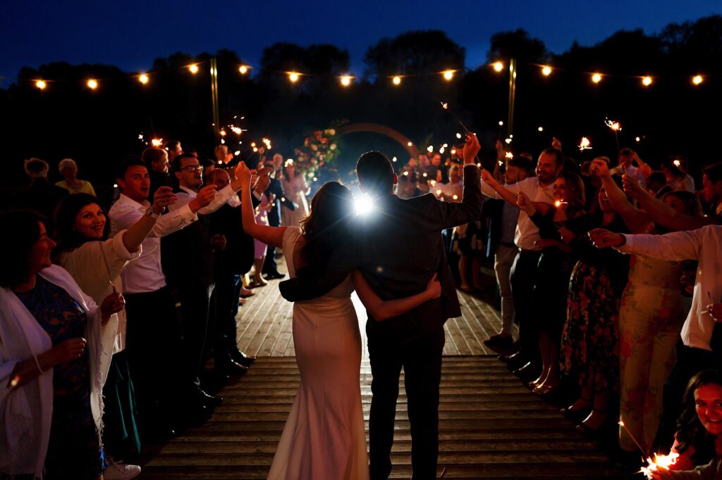 Wedding couple walking away waving sparklers with their guests