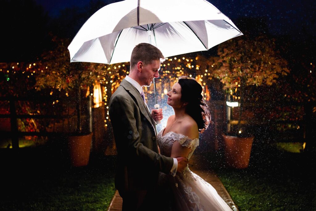 Bride and groom looking at each other under an umbrella with rain backlit