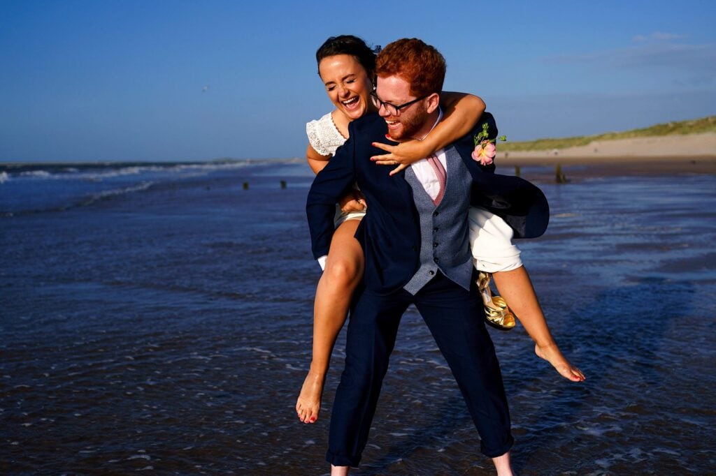 Bride having a piggyback on beach whilst laughing