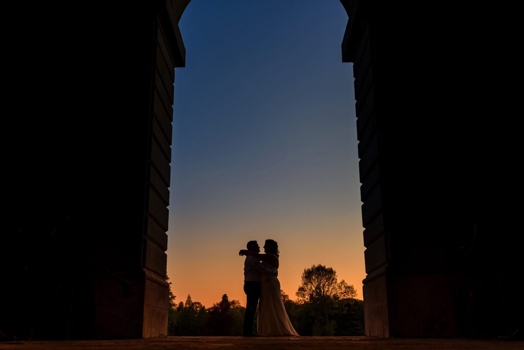 Wedding couple under arch at sunset in a Cambridge College