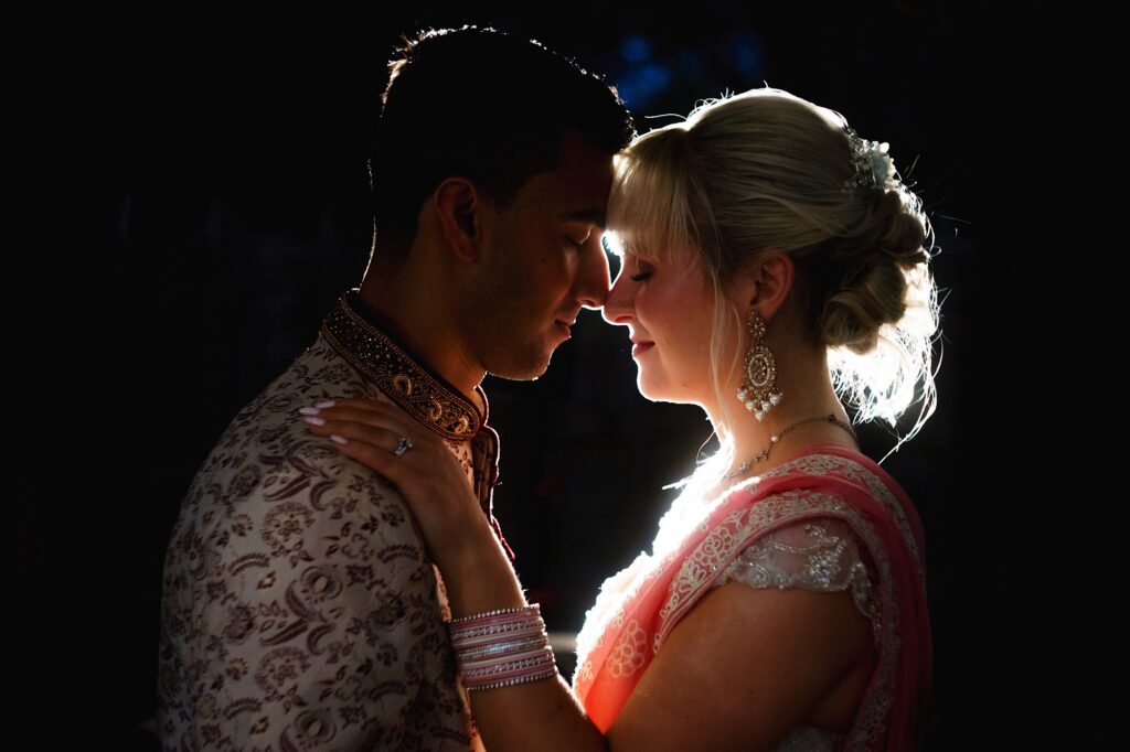 Bride and groom in Asian wedding clothes backlit at night