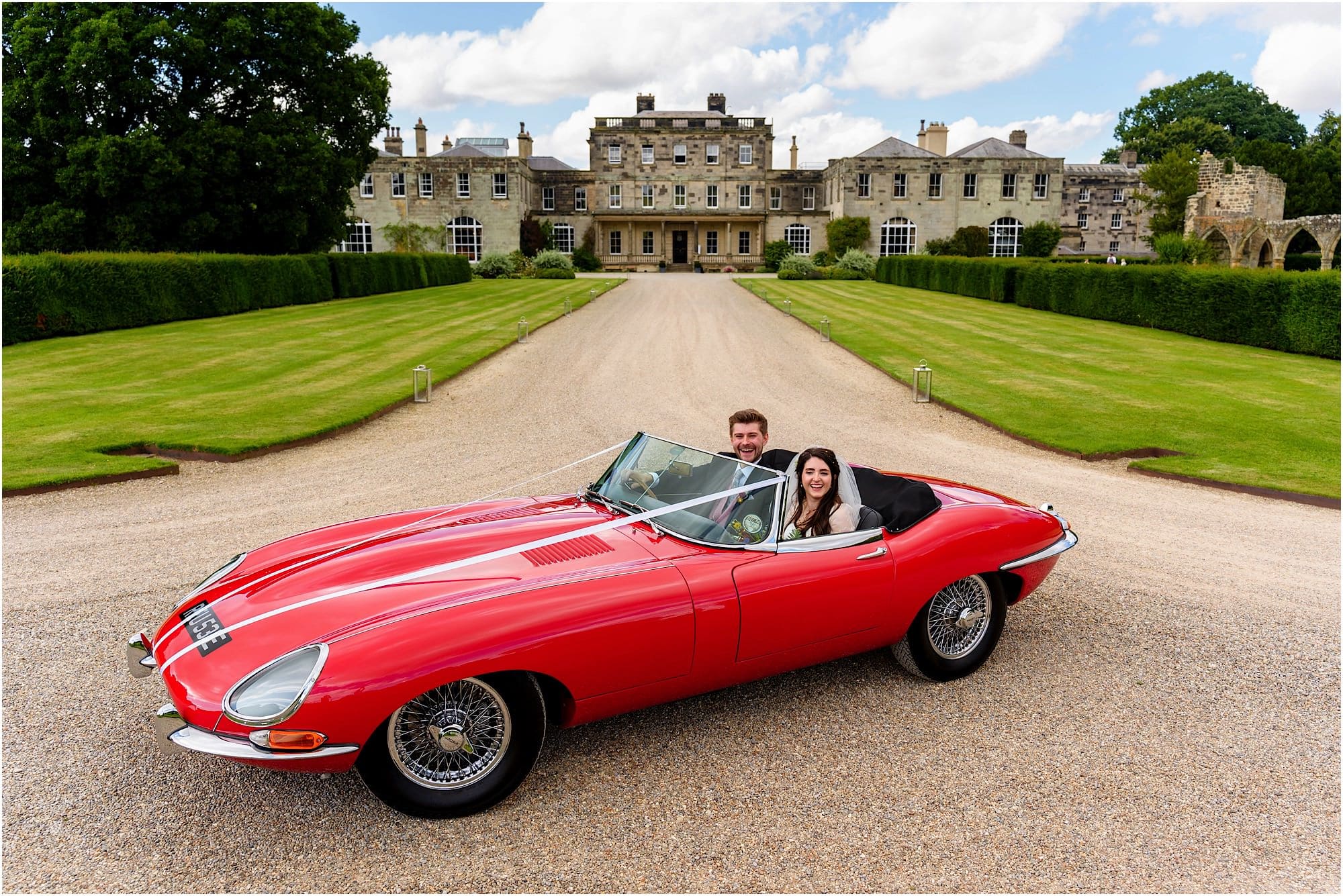 Bride and groom in red e-type jag in front of Birdsall House